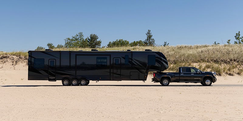 A black 2024 GMC Sierra 3500 HD parked with a massive RV hitched to the back
