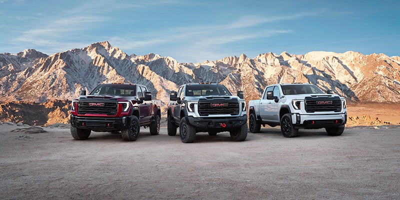 A red, black, and white GMC Sierra 2500 HD pickup truck parked in a row with a mountain range in the background