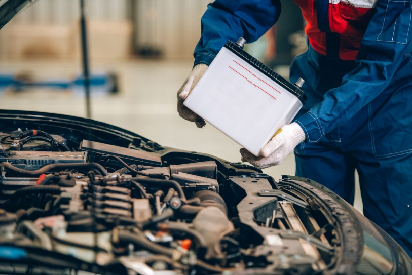 Mechanic installing or replacing a car battery under the vehicle hood.